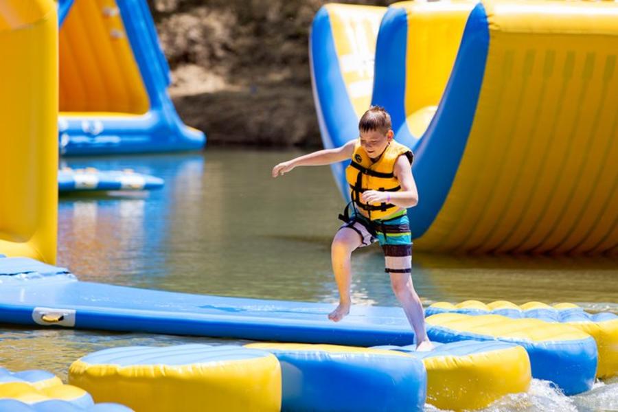 child jumping on floating cushions on a lake, while wearing a life jacket