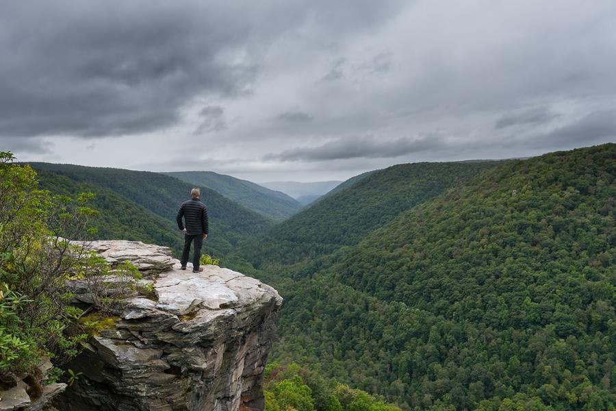 man standing at edge of cliff overlooking mountains
