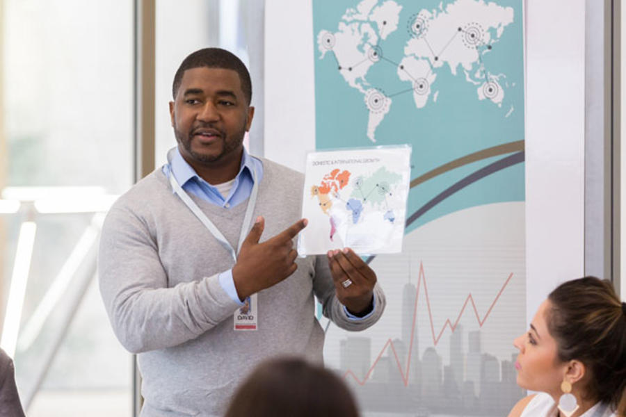 Man making presentation to group as he gestures toward chart