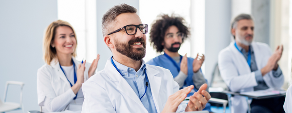 Medical professionals sitting at desks in conference presentation, clapping
